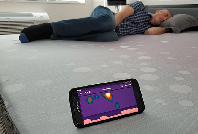 man lying on the ReST smart bed with the phone App showing the live pressure mapping