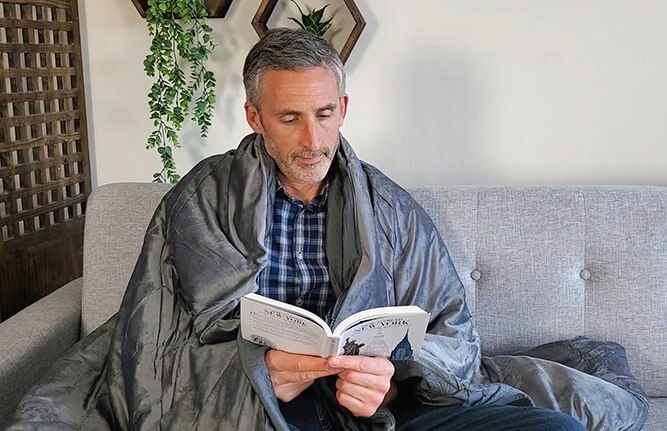 man using the luxome weighted blanket on the sofa while reading a book